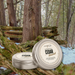 Two tins of 'Cedar Harvest' wax melts on a natural background with trees and logs.