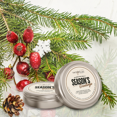 Two tins of 'Season's Greetings' candle with Christmas decorations on a white background